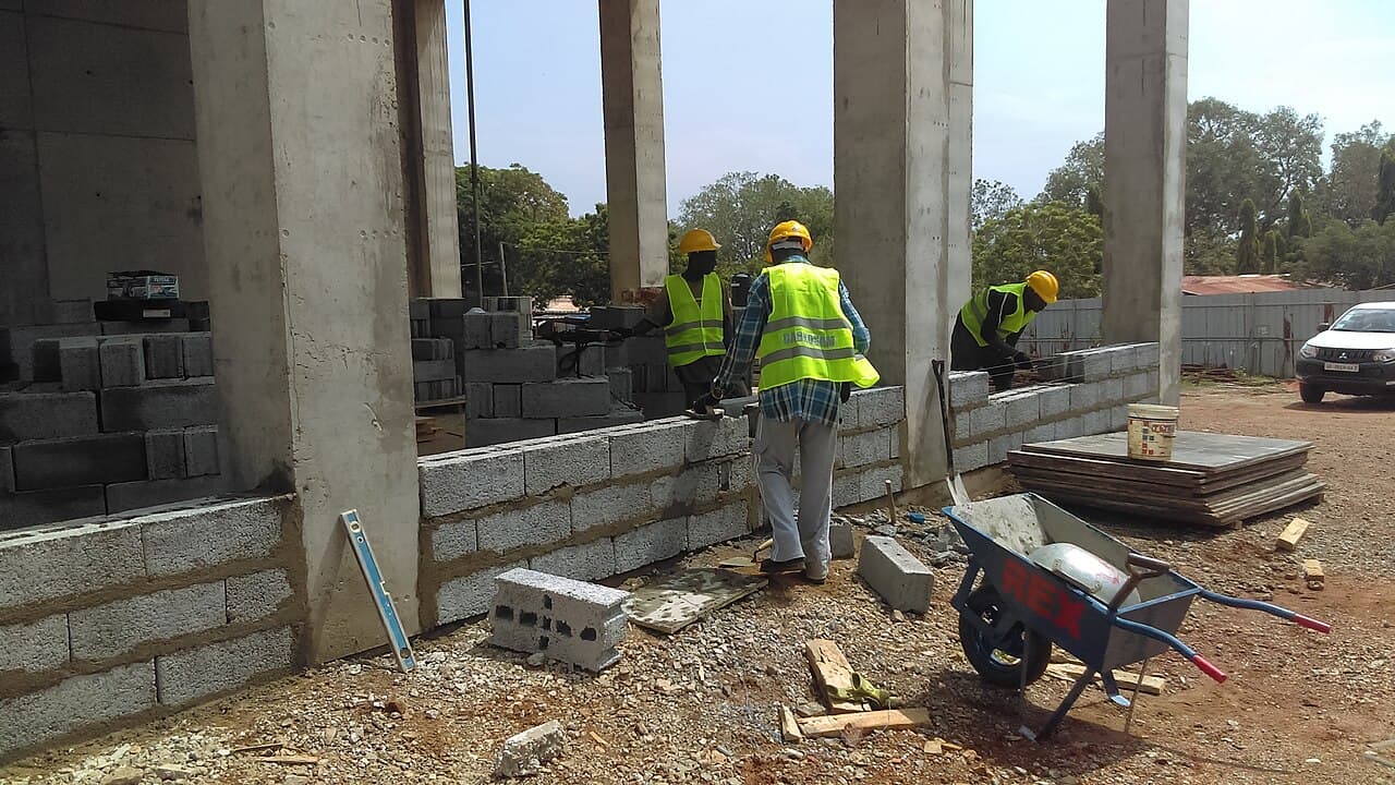 A building crew laying blockwork on a site in Ghana, supervised on the spot.