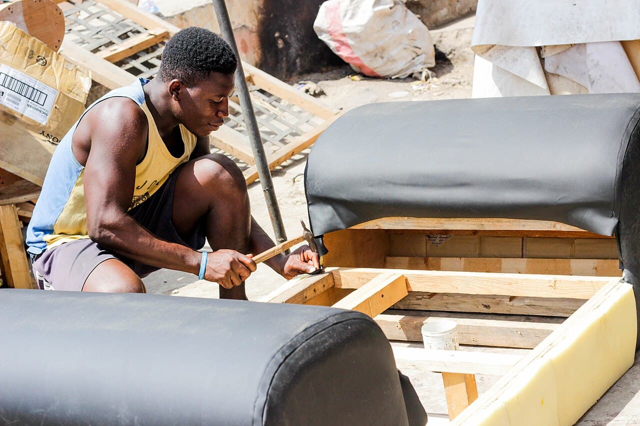 A carpenter hammering a hardwood frame for a sofa in an open workshop.